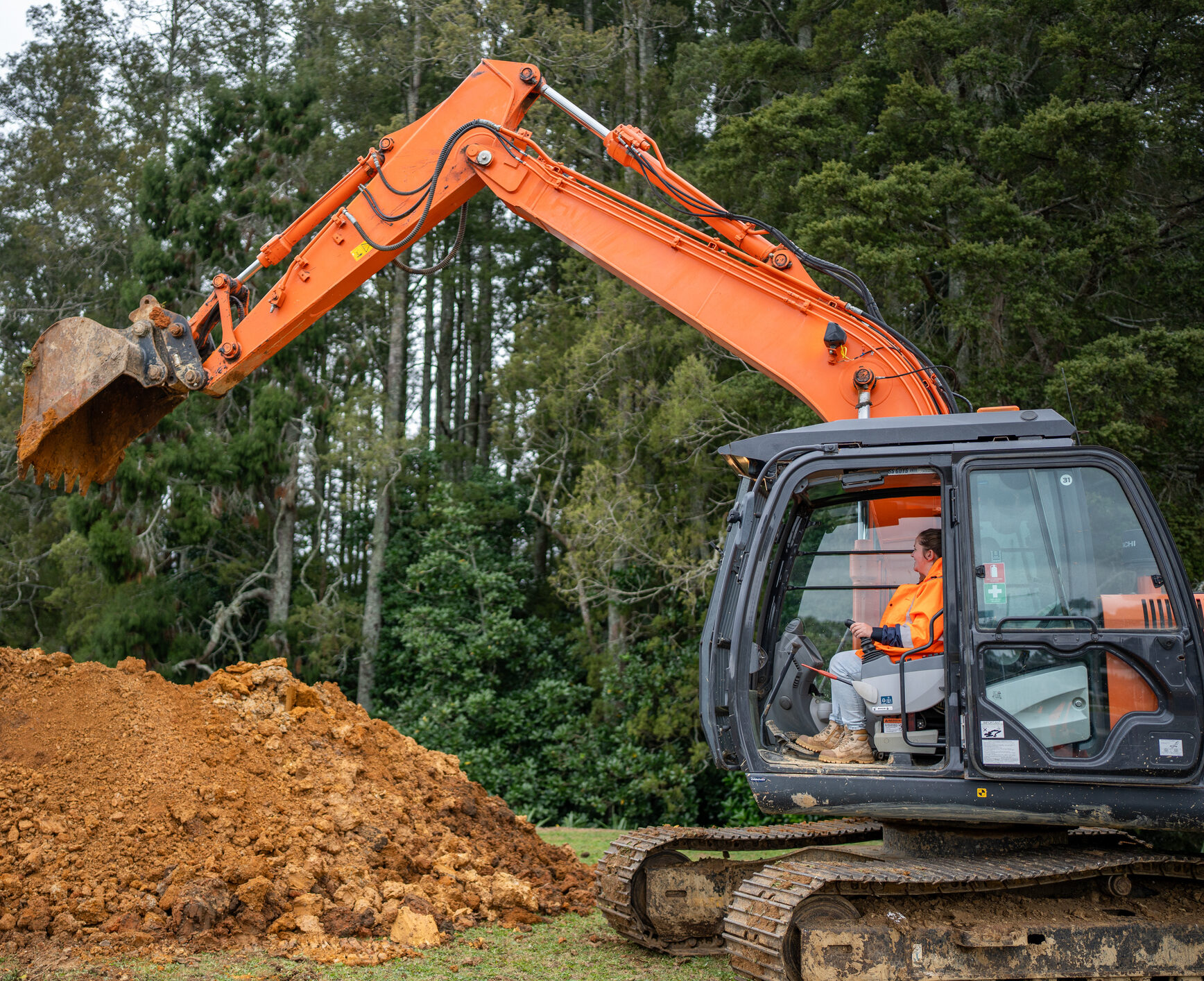 A worker operates a large orange excavator to lift and move soil